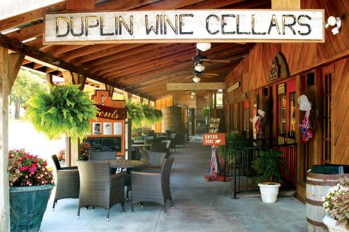 Exterior view of Duplin Wine Cellars featuring a porch with seating, plants, and decorative signage.