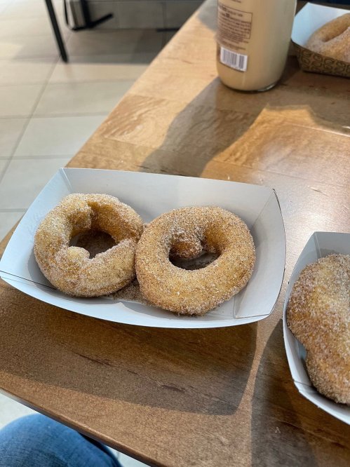 Two cinnamon sugar donuts on a paper tray, resting on a wooden table.