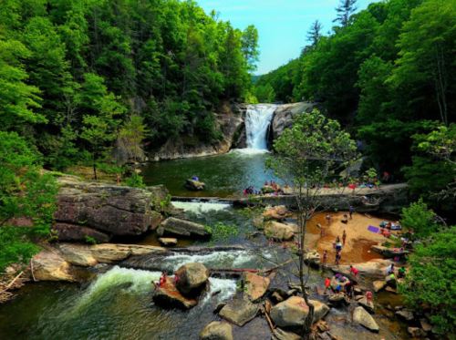 A scenic waterfall surrounded by lush greenery, with people enjoying the water and sunbathing on the rocks.