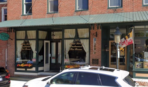A charming brick building with large windows displaying "Enchanted Tea Room" signage and flower boxes.