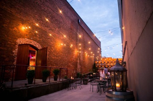 Outdoor venue with string lights, brick walls, and tables set for an event, creating a warm, inviting atmosphere.