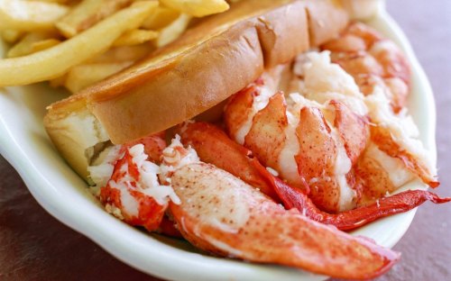 A close-up of a lobster roll filled with chunks of lobster meat, served with a side of French fries.