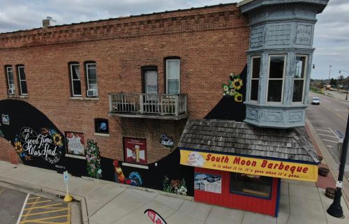 A colorful mural on a brick building featuring a balcony and a barbecue restaurant with a sign.