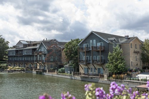 A scenic view of a waterfront hotel with balconies, surrounded by greenery and flowers under a cloudy sky.
