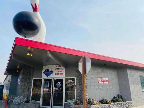 A bowling alley with a large bowling pin sign, featuring a red roof and "Open" sign on the door.