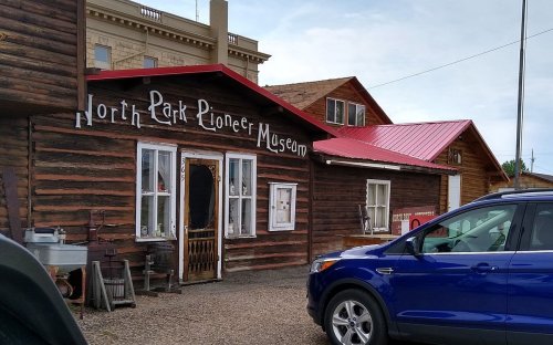 Exterior of the North Park Pioneer Museum, featuring a wooden facade and a red roof, with a blue car parked nearby.