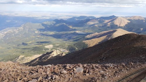 A panoramic view of mountains and valleys under a cloudy sky, showcasing rugged terrain and distant peaks.