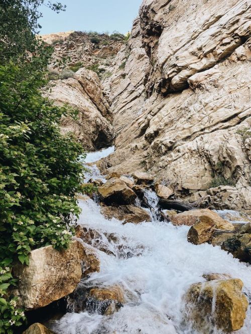 A cascading waterfall flows over rocky terrain, surrounded by lush greenery and steep cliffs.