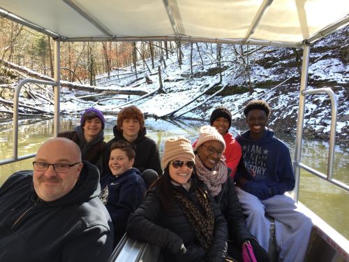 A group of eight people on a boat, smiling, surrounded by snowy trees and water.