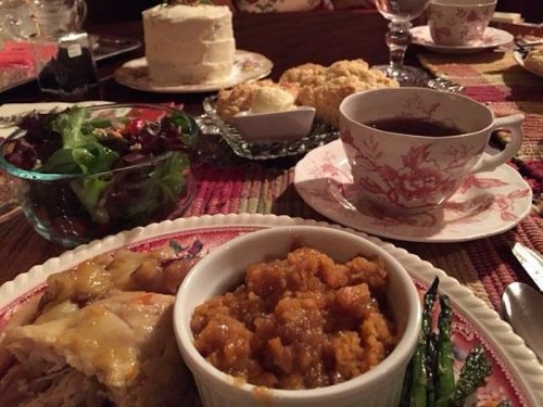 A beautifully set table with a variety of dishes, including salad, roasted chicken, squash, scones, and tea.