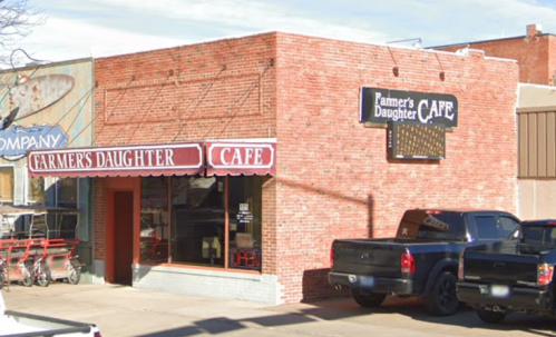 A brick building with a sign reading "Farmer's Daughter Cafe" and parked trucks outside.