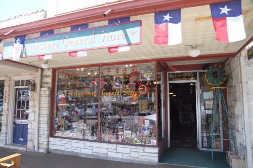A charming general store with a stone facade, colorful decorations, and Texas flags adorning the entrance.