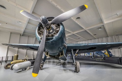 A vintage aircraft with a large propeller displayed in a museum, showcasing its detailed engine and wings.