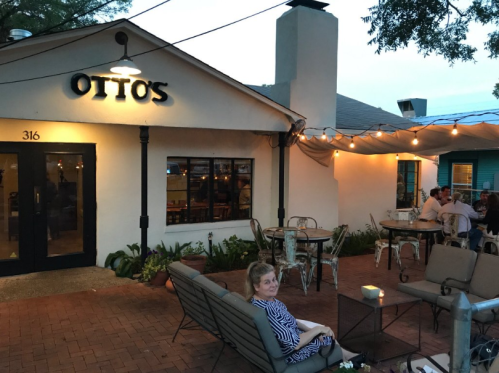 A cozy outdoor dining area at Otto's, with string lights and guests enjoying the evening. A woman sits in the foreground.