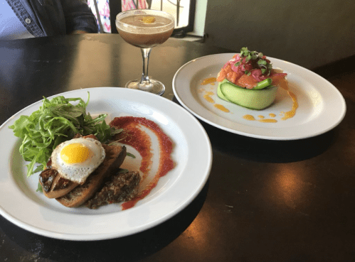 A plate with a small salad, toast topped with an egg, and sauce, alongside a cucumber dish with salmon and garnish.