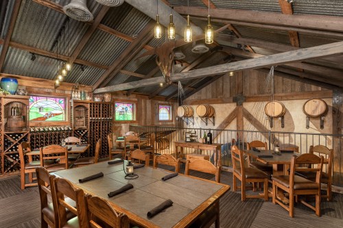 Cozy rustic restaurant interior with wooden tables, wine storage, and stained glass windows. Warm, inviting atmosphere.