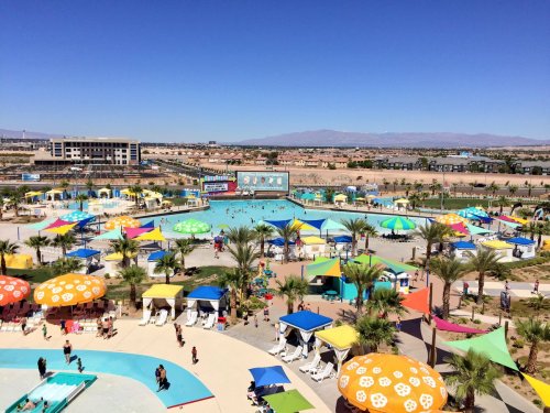 A vibrant water park with colorful umbrellas, pools, and palm trees under a clear blue sky.