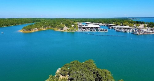Aerial view of a serene lake surrounded by greenery, with marinas and boats visible along the shoreline.