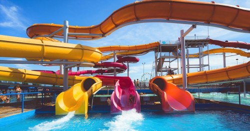 Colorful water slides twist and turn above a pool, with people enjoying the water on a sunny day.