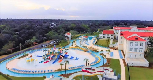 Aerial view of a large water park with slides, pools, and colorful play areas surrounded by greenery and buildings.