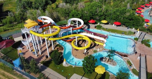 Aerial view of a colorful water park with slides, a lazy river, and lounge areas surrounded by greenery.