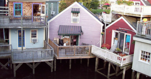 Colorful houses on stilts over water, featuring porches and flower pots, creating a charming waterfront scene.