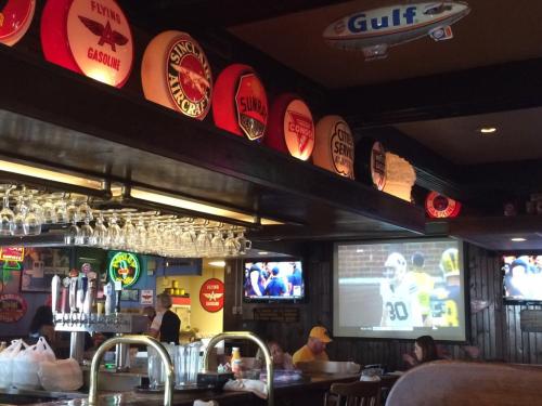A cozy bar interior featuring vintage gas station signs, a large TV showing a sports game, and a well-stocked bar.