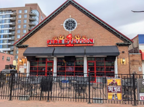Exterior of Fire Station restaurant and brewing co., featuring a brick facade and large windows, with outdoor seating.