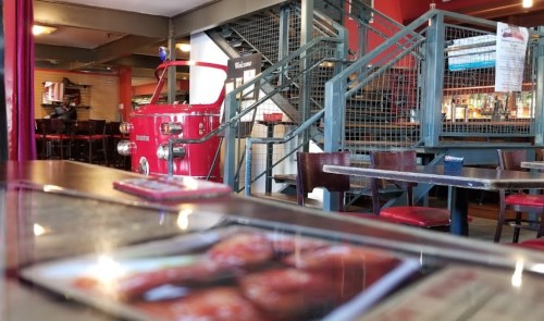 Interior of a restaurant featuring a red vintage vehicle, stairs, and tables with menus in the foreground.