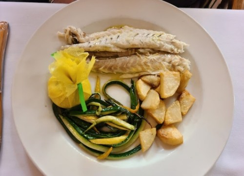 A plate with cooked fish, yellow pouch, sautéed zucchini, and roasted potatoes.