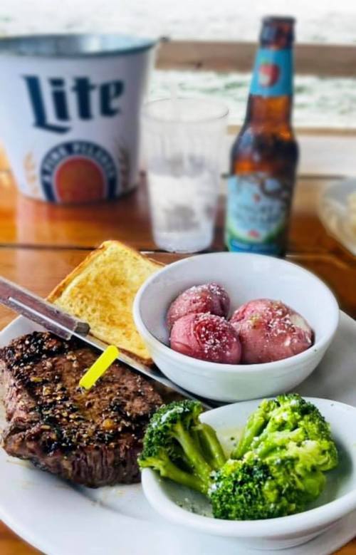 A plate with steak, broccoli, and potatoes, accompanied by toast and a beer in the background.