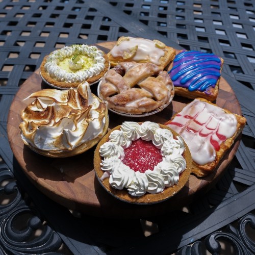 A wooden platter with an assortment of colorful pastries and pies, featuring various toppings and fillings.