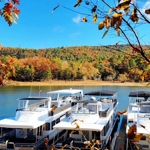 Boats docked by a calm lake, surrounded by vibrant autumn foliage and a clear blue sky.