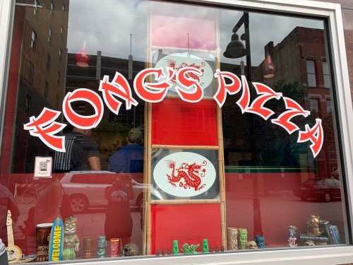 Sign for Fong's Pizza displayed in a window, featuring a dragon design and colorful decor below.
