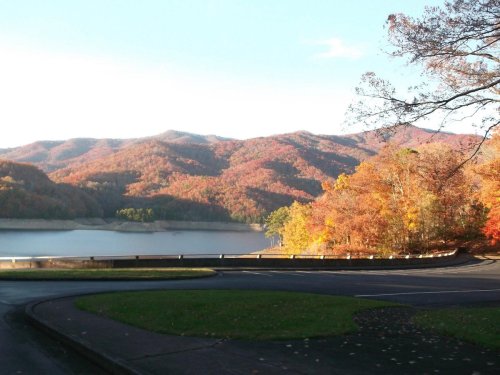 Scenic view of colorful autumn foliage on mountains beside a calm lake under a clear blue sky.