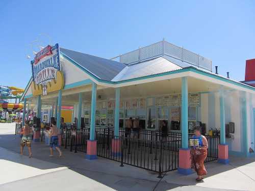 A colorful snack stand with a blue roof, surrounded by people enjoying a sunny day at a water park.