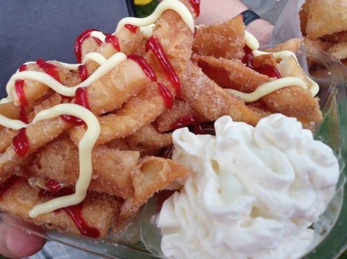 A close-up of crispy fried snacks drizzled with ketchup and mayonnaise, served with a dollop of whipped cream.