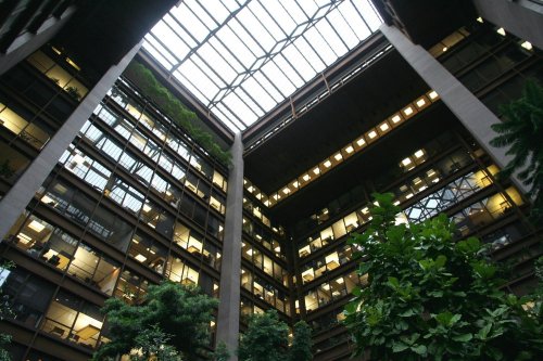 A modern atrium with glass ceiling, surrounded by multiple floors of offices and lush indoor plants.