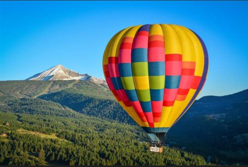 A colorful hot air balloon floats over a green landscape with a snow-capped mountain in the background.