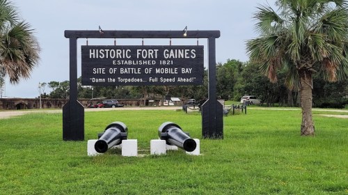 Sign for Historic Fort Gaines, established 1821, with two cannons in front, marking the site of the Battle of Mobile Bay.