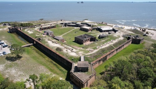 Aerial view of a historic fort surrounded by water, featuring buildings and grassy areas within its walls.