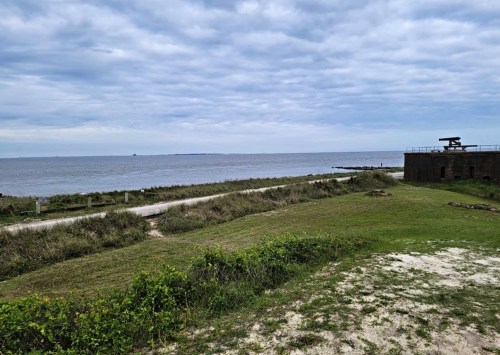A coastal view featuring grassy land, a path, and a calm sea under a cloudy sky.