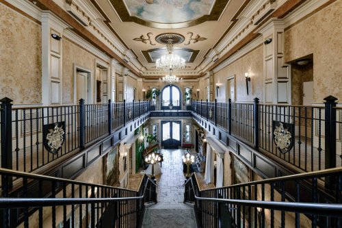 Elegant staircase in a grand hallway with ornate decor, chandeliers, and large windows.