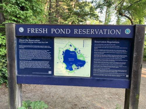Sign for Fresh Pond Reservation, detailing regulations and a map of the area, surrounded by trees.