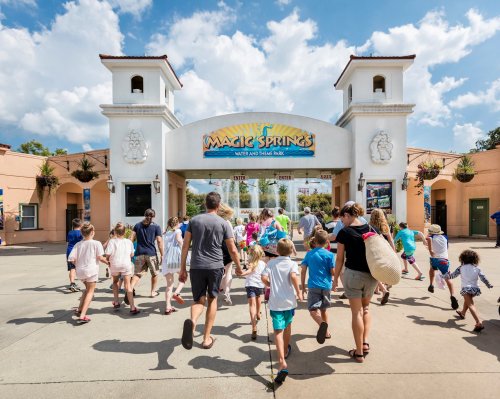 A group of families and children entering the Magic Springs water and theme park on a sunny day.