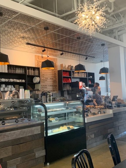 A cozy café interior with a counter, display case, and a barista at work under stylish pendant lights.
