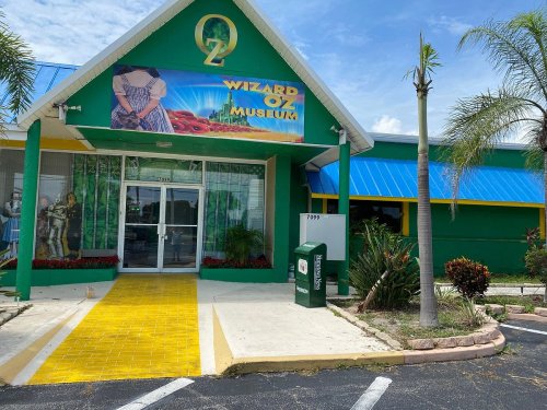 Exterior of the Wizard of Oz Museum, featuring a colorful facade and a yellow brick road pathway. Palm trees in view.
