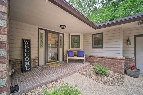 A welcoming porch with a bench, "WELCOME" sign, and greenery, surrounded by a brick pathway and flower beds.