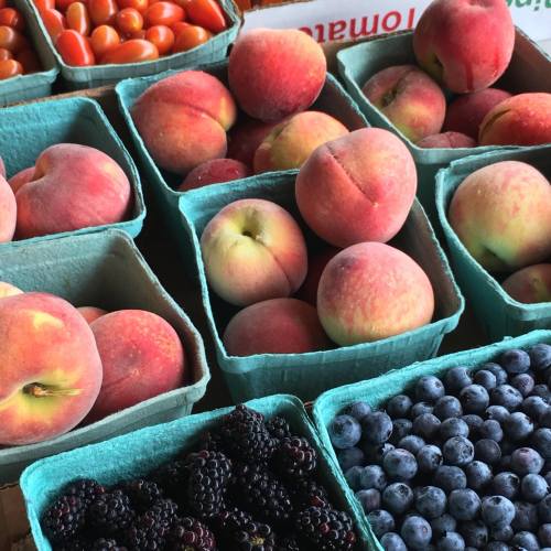 Baskets of fresh peaches, plums, blackberries, and cherry tomatoes at a market.