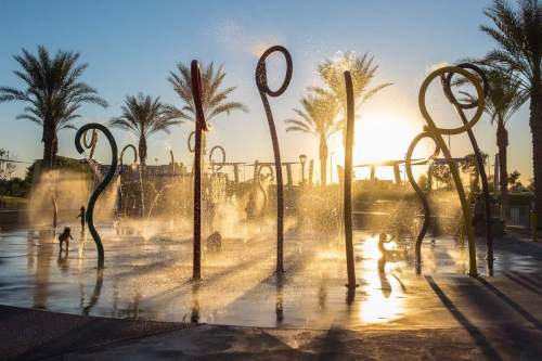 A sunlit splash pad with playful water features and palm trees, creating a vibrant scene at sunset.